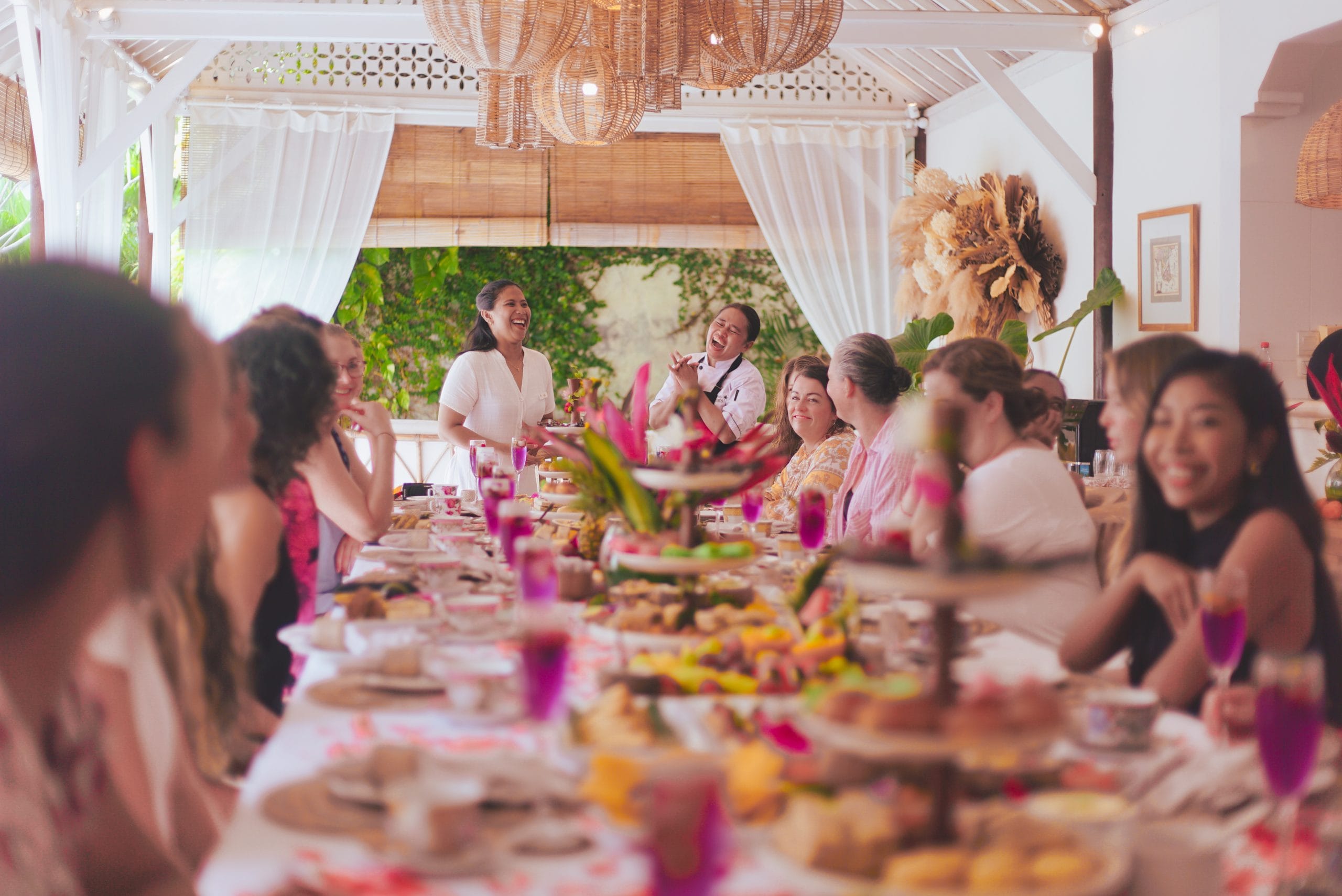 Guests enjoying a luxurious high tea experience surrounded by lush tropical greenery at a Goddess Retreat, featuring elegant table settings, delicious treats, and a serene ambiance.